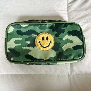 May include: A green camouflage makeup bag with a yellow smiley face patch.