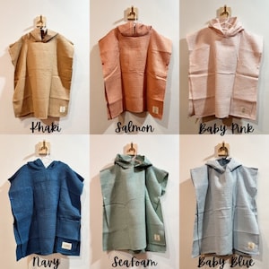 May include: Six hooded towels in different colors: khaki, salmon, baby pink, navy, seafoam, and baby blue. The towels are made of waffle weave fabric and have a hood with a button closure.