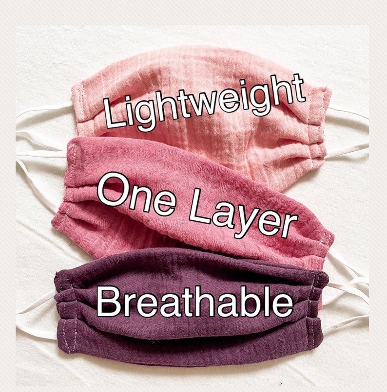 May include: Three pink and purple fabric face masks with white elastic ear loops. The top mask has the text "Lightweight" printed on it. The middle mask has the text "One Layer" printed on it. The bottom mask has the text "Breathable" printed on it.