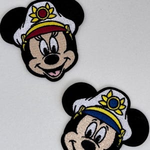 May include: Two embroidered patches featuring cartoon mouse faces with black ears and smiling expressions. Each mouse wears a white hat with a yellow and red floral design. One hat has a red brim, the other has a blue brim.