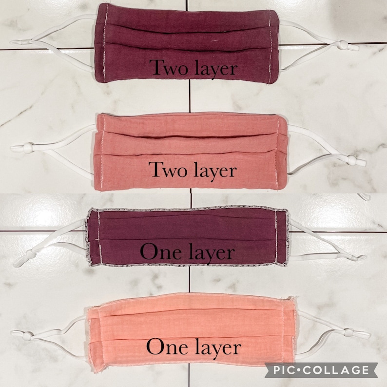 May include: Four fabric face masks, two in a darker pink and two in a lighter pink. The masks are pleated and have white elastic ear loops. The text "Two layer" is printed on the top two masks and "One layer" is printed on the bottom two masks.