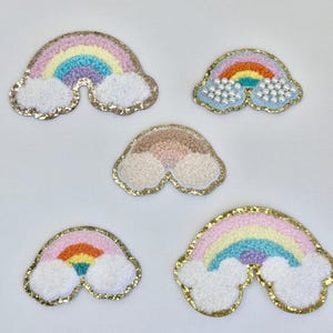 May include: Five rainbow patches with fluffy clouds. The rainbows are embroidered with colorful yarn and have a gold glitter outline. Some of the clouds have pearl beads.
