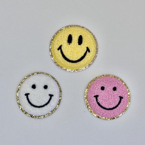 May include: Three embroidered smiley face patches with gold glitter trim. The smiley faces are yellow, white, and pink.