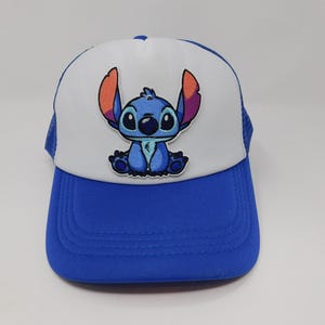 May include: A blue and white trucker hat featuring a cartoon image of Stitch. The hat has a blue brim and mesh back, with a white front panel displaying the character. The Stitch graphic is blue with orange ears.