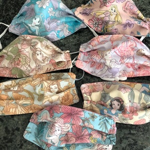 May include: Set of six colorful fabric face masks featuring different Disney princesses. Each mask has a floral pattern and a different princess image. The princesses include Ariel, Belle, Cinderella, Snow White, Rapunzel, and Jasmine.