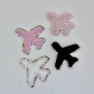 Puede incluir: Cuatro parches de avión de fieltro en diferentes colores y estilos. Uno es rosa con detalles de perlas blancas, otro es blanco con detalles dorados, uno es negro con detalles dorados y otro es rosa con detalles dorados.