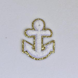 May include: White anchor with a gold glitter outline. The anchor is a popular nautical symbol.