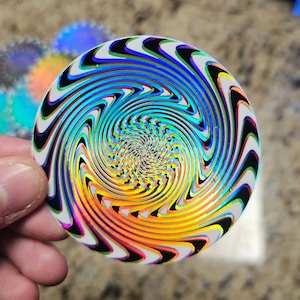 May include: A round, iridescent sticker with a swirling, hypnotic pattern in shades of blue, green, yellow, orange, and black.
