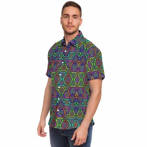 Puede incluir: Camisa de manga corta con un vibrante estampado geométrico en tonos verdes, azules, morados, naranjas y amarillos. La camisa tiene un cuello clásico y cierre de botones. El diseño es un patrón repetitivo de formas interconectadas.