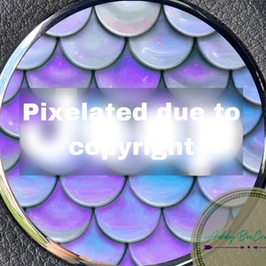 Pu&ograve; includere: Primo piano di un design rotondo di squame di sirena iridescenti di colore viola e blu. L'immagine &egrave; pixelata a causa dei diritti d'autore.