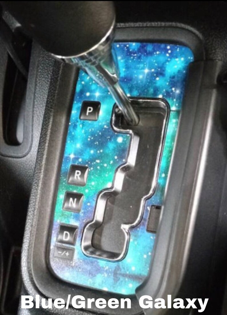 May include: A blue and green galaxy-themed car gear shift plate with the letters "P", "R", "N", "D", and "+/-" printed on it.