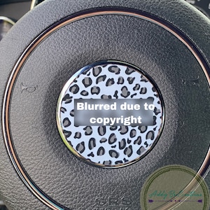 May include: A black leather steering wheel with a silver trim and a leopard print design in the centre. The centre design is blurred due to copyright. The text "Addy B Creations" is visible in the bottom right corner.