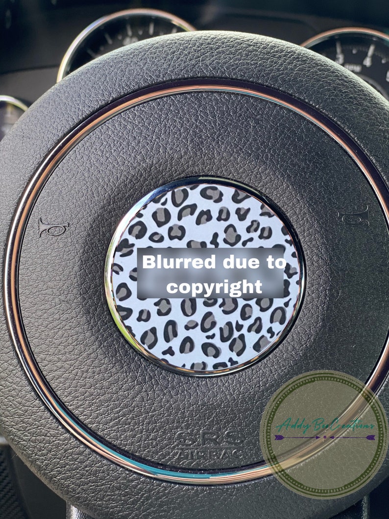 May include: A black leather steering wheel with a silver trim and a leopard print design in the centre. The centre design is blurred due to copyright. The text "Addy B Creations" is visible in the bottom right corner.