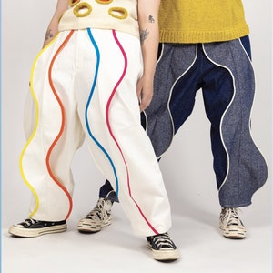 Puede incluir: Dos pantalones únicos. Un par es blanco con ribetes ondulados y coloridos en amarillo, rojo y azul. El otro par es azul vaquero con ribetes ondulados blancos. Ambos pares se usan con zapatillas.