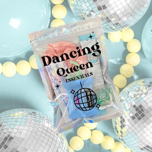 Pode incluir: Uma bolsa transparente com a inscrição "Dancing Queen Essentials" contém um elástico de cabelo rosa e um pacote azul com um desenho de bola de discoteca. O fundo apresenta bolas de discoteca, esferas azul claro e contas amarelas.