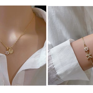 May include: A gold necklace with a small flower charm and a round pendant. A gold bracelet with a flower charm and a letter charm.