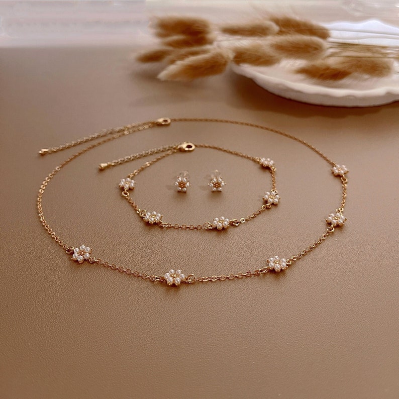 Peut inclure: Un ensemble de bijoux en or compos&eacute; d'un collier fin, d'un bracelet assorti et d'une paire de boucles d'oreilles. Chaque pi&egrave;ce est orn&eacute;e de petites fleurs blanches en perles.
