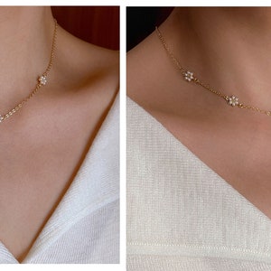 Peut inclure: Un collier d&eacute;licat en cha&icirc;ne dor&eacute;e avec de petits pendentifs en forme de fleur. Le collier est pr&eacute;sent&eacute; sur un mannequin portant une chemise blanche.