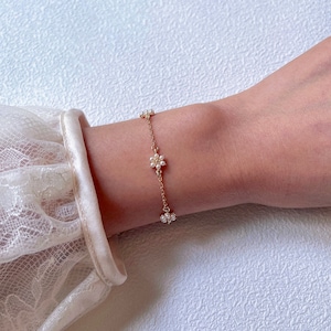 Peut inclure: Un bracelet d&eacute;licat en cha&icirc;ne dor&eacute;e avec de petites fleurs en perles.