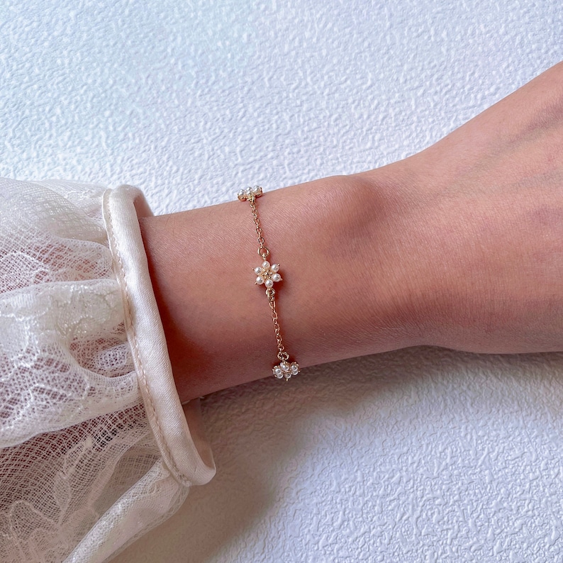 Peut inclure: Un bracelet d&eacute;licat en cha&icirc;ne dor&eacute;e avec de petites fleurs en perles.