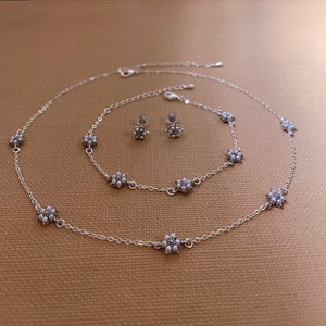 Peut inclure: Un ensemble de bijoux en argent compos&eacute; de trois cha&icirc;nes d&eacute;licates avec des breloques en forme de fleurs et une paire de boucles d'oreilles assorties. Les cha&icirc;nes sont superpos&eacute;es et pr&eacute;sentent un design simple et &eacute;l&eacute;gant.