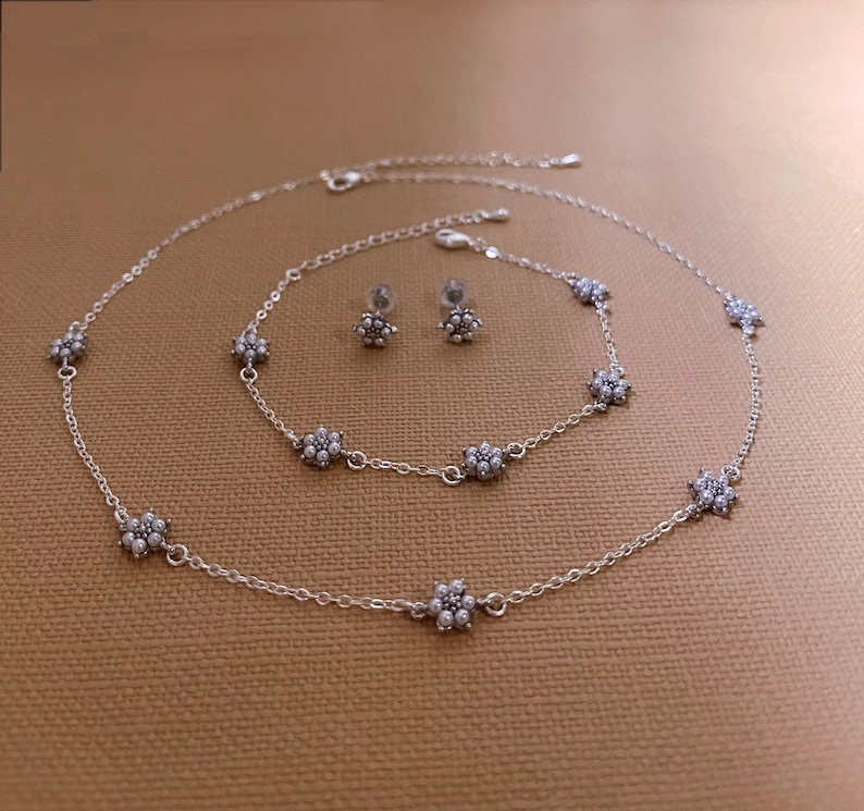 Peut inclure: Un ensemble de bijoux en argent compos&eacute; de trois cha&icirc;nes d&eacute;licates avec des breloques en forme de fleurs et une paire de boucles d'oreilles assorties. Les cha&icirc;nes sont superpos&eacute;es et pr&eacute;sentent un design simple et &eacute;l&eacute;gant.