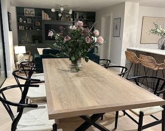 May include: A light wood dining table with a black metal base, surrounded by black chairs with woven seats. A vase of pink roses sits in the center. The room has a modern design with a built-in entertainment center and a bar area.