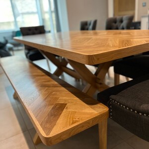 May include: A wooden dining table and bench set with a herringbone pattern. The table has a natural wood finish and the bench has a light wood finish. The table is surrounded by chairs with dark upholstery.