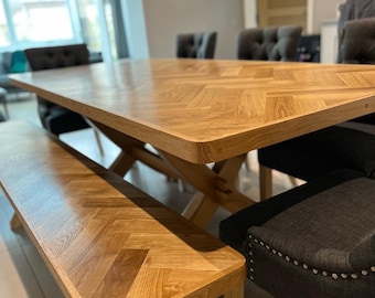 May include: A wooden dining table with a herringbone pattern top and a matching bench. The table is surrounded by chairs with dark gray upholstery and silver studs.
