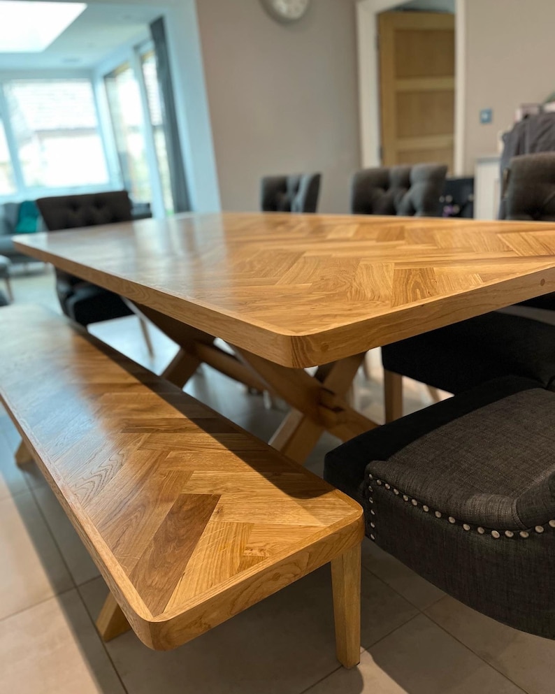 May include: A wooden dining table with a herringbone pattern top and a matching bench. The table is surrounded by chairs with dark grey upholstery and silver studs.