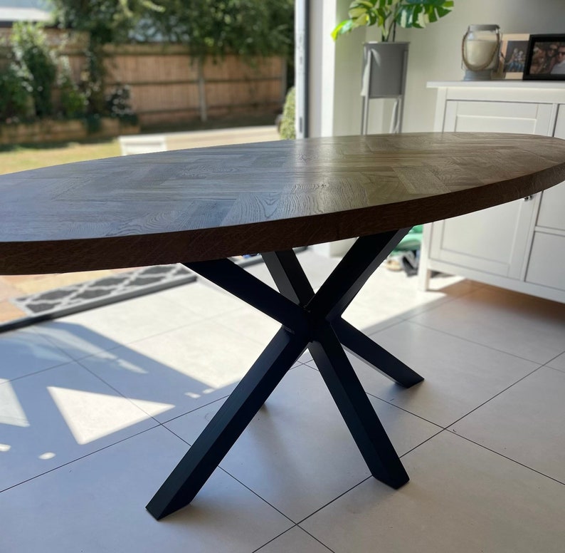 May include: Oval wooden dining table with a black metal base. The table top has a herringbone pattern and a glossy finish.