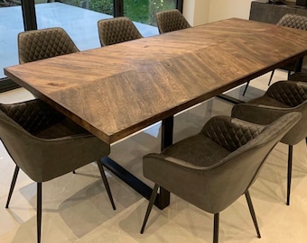 May include: A large wooden dining table with a chevron pattern and a black metal base. The table is surrounded by six dark gray upholstered chairs with black metal legs.
