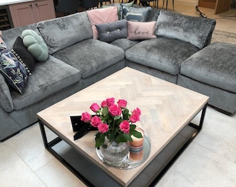 May include: A gray sectional sofa with a variety of pillows, including a pink pillow with the word "love" on it. A coffee table with a light wood top and black metal frame sits in front of the sofa. A vase of pink roses sits on the coffee table.