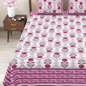 Puede incluir: Una sábana de cama blanca y rosa con estampado floral y un borde rosa. La sábana está en una cama con dos fundas de almohada a juego con estampado floral rosa.