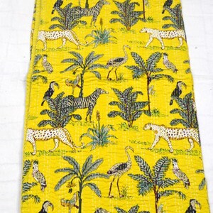 May include: Yellow fabric featuring a jungle-themed pattern with zebras, leopards, birds, and palm trees. The design has a hand-stitched look. The material is likely cotton or a similar fabric, suitable for various uses.