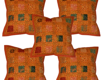 May include: Set of five orange and green patterned throw pillows with a red border. The pillows are made of a patchwork fabric with a variety of designs.