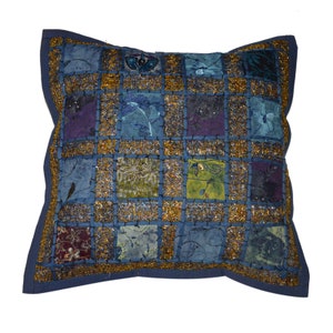 Puede incluir: Una almohada de tiro de patchwork azul y dorado con un patrón cuadrado. La almohada está hecha de diferentes telas y tiene un ribete dorado decorativo.