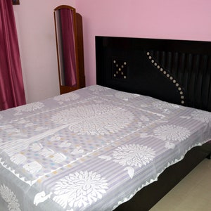 Op de afbeelding: Een wit bedovertrek met een bloemenpatroon op een zwart bedframe met een decoratief hoofdeinde. Het bed staat in een kamer met roze muren en een spiegel.