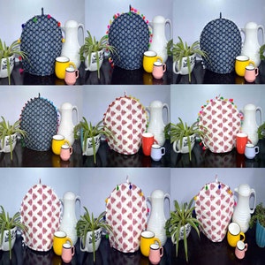 May include: Nine tea cozy covers with pom-pom trim. The covers are in three different patterns: blue and white, red and white, and white with a red and blue pattern. The covers are displayed on top of white teapots with matching mugs.