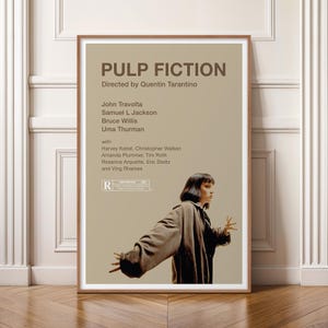 K&ouml;nnte beinhalten: Ein gerahmtes Filmplakat f&uuml;r "Pulp Fiction" mit einem braunen Holzrahmen. Das Plakat zeigt den Filmtitel, den Regisseur und die Besetzung, darunter John Travolta und Uma Thurman. Das Bild zeigt eine Frau in einem braunen Mantel.