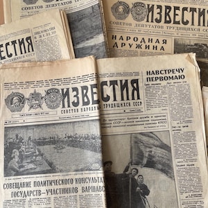 May include: A selection of aged newspapers with Cyrillic script, including the word "Izvestia" in the mastheads, alongside Soviet emblems. The papers show signs of age, with visible wear and tear, and contain various articles and headlines.