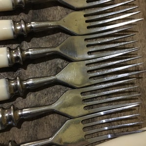 May include: Set of six silver forks with ivory handles. The forks have a traditional design with a rounded handle and a pointed end.