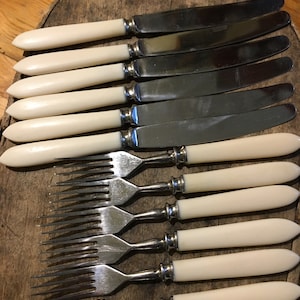 May include: A set of six silver forks and six silver knives with ivory-colored handles. The cutlery is arranged in a row on a wooden surface.