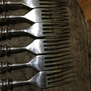 May include: Set of six silver forks with white handles. The forks are arranged in a row, with the tines facing up. The forks are on a wooden surface.
