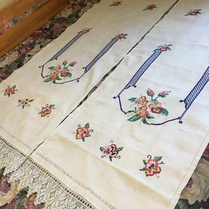 Pode incluir: Dois caminhos de mesa de linho branco com desenhos florais bordados e detalhes azuis. Os caminhos de mesa têm uma borda de renda de crochê.