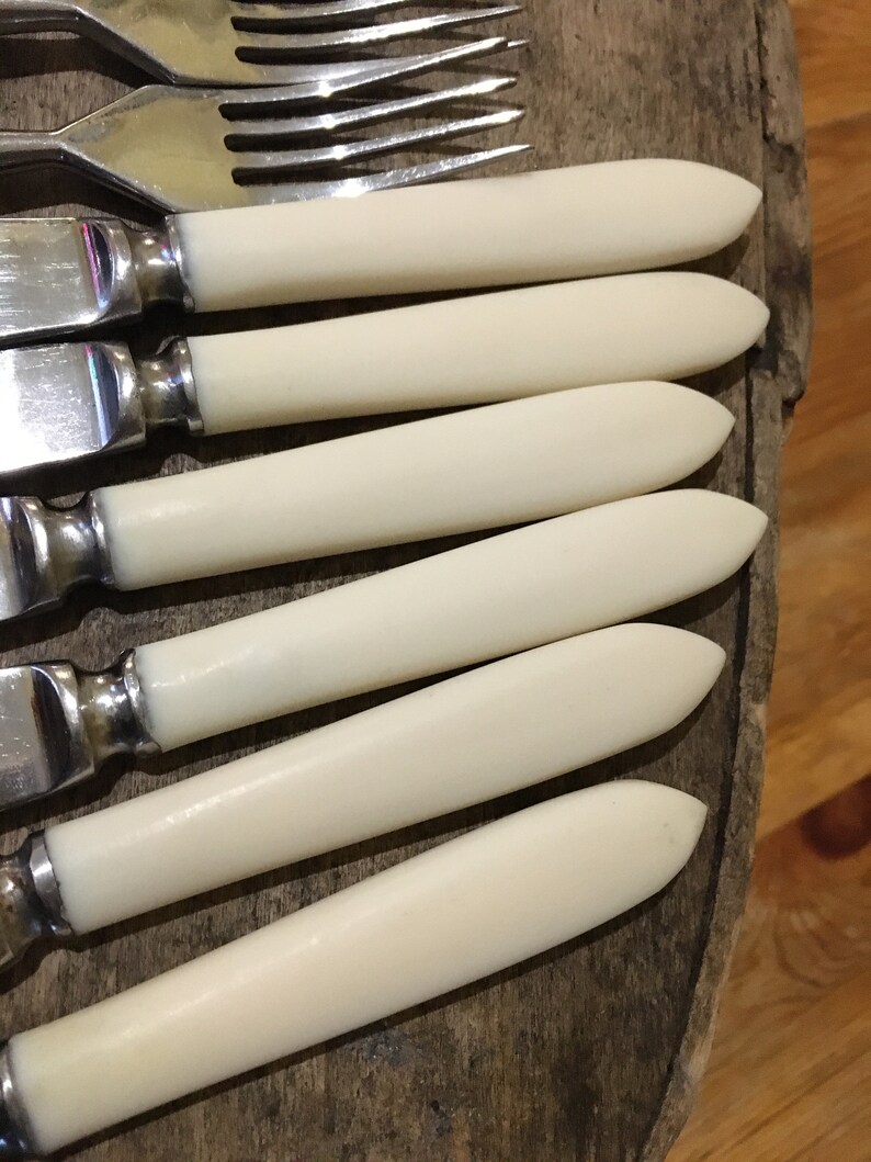 May include: Set of six silver knives with white bone handles. The knives are arranged in a row, with the handles facing the viewer.