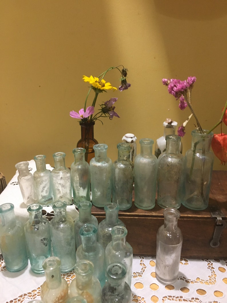 May include: A collection of small, clear glass bottles with a variety of flowers in them. The bottles are arranged in a row on a wooden surface. The flowers are yellow, pink, and purple.