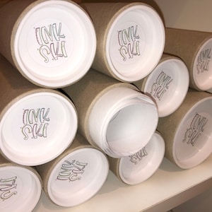 May include: Close-up of several brown cardboard tubes with white end caps. Each end cap has a white circle with the text "INK SKI" in black lettering.