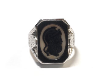 Puede incluir: Un anillo de plata con un camafeo negro que presenta el perfil de una persona con un casco. El anillo tiene un diseño detallado alrededor del camafeo.