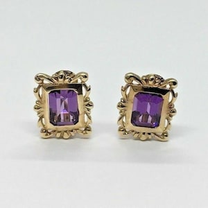 Könnte beinhalten: Ein Paar goldene Ohrringe mit violetten Amethyst-Edelsteinen, die in verzierten Rahmen gefasst sind.